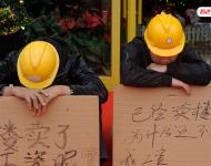 2012年12月25日，廣東中山，火炬開發(fā)區(qū)的多名建筑工人討要工作一年多的血汗錢一籌莫展，一些工人干脆將鋪蓋卷搬到了售樓部，并在門口搭起灶臺(tái)煮飯，希望以這種方式討回工錢。圖為在銷售中心門外，工人舉牌討薪。吳進(jìn)/視覺中國(guó)